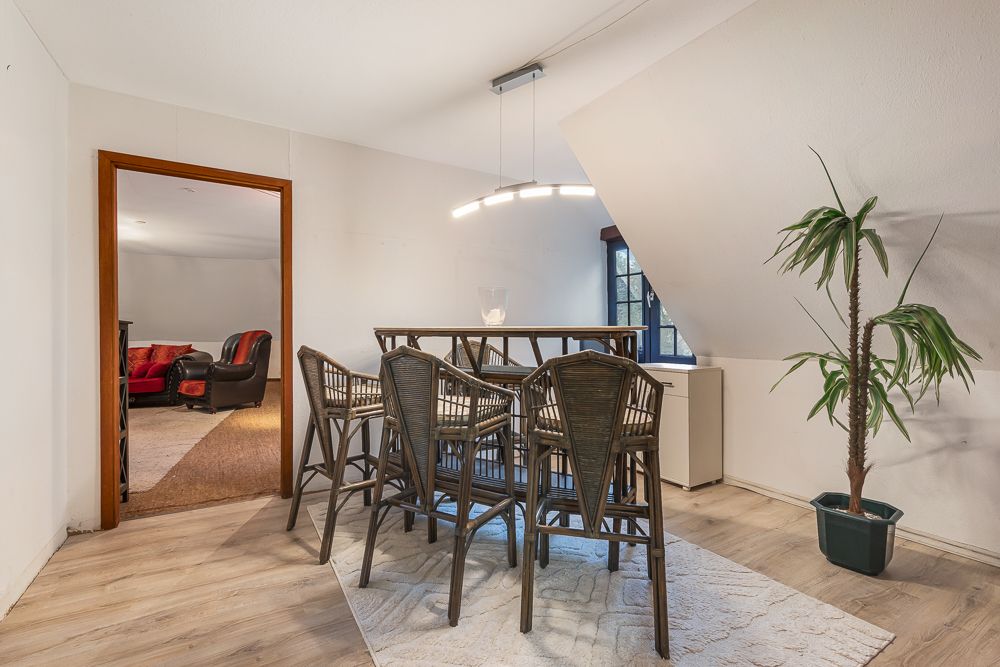 Essbereich mit Holztisch, sechs Stühlen, Teppich und Pflanze, angrenzend an ein Wohnzimmer.