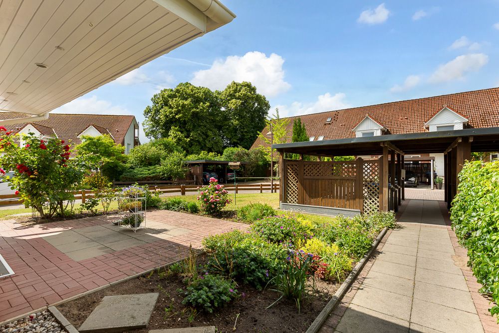 Gepflegter Garten mit Terrasse, Blumenbeeten und überdachtem Holzpavillon vor Wohnhäusern.
