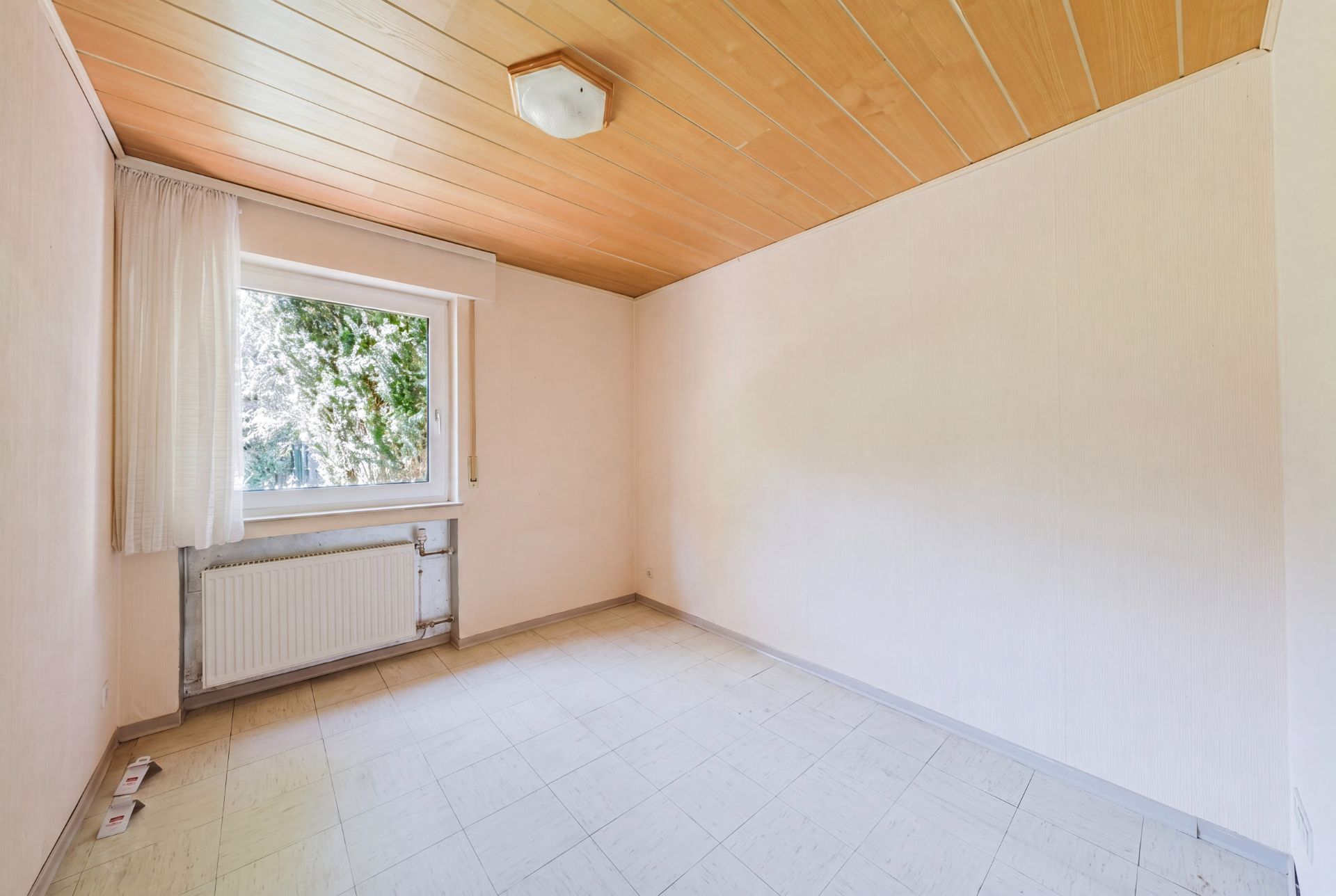 Leeres Zimmer mit Fenster, Heizkörper und Holzdecke.