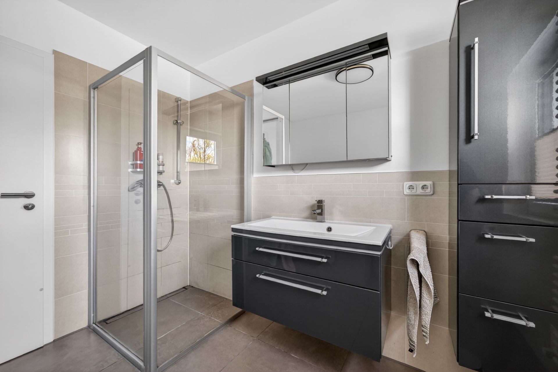 Modernes Badezimmer mit Dusche, Spiegel, Waschbecken und schwarzen Schränken.