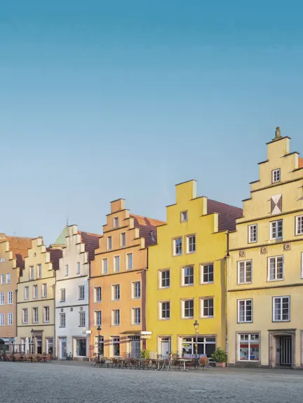 Mehrere bunte Wohnhäuser mit Stufengiebeln an einem Platz, davor stehen Tische und Stühle.