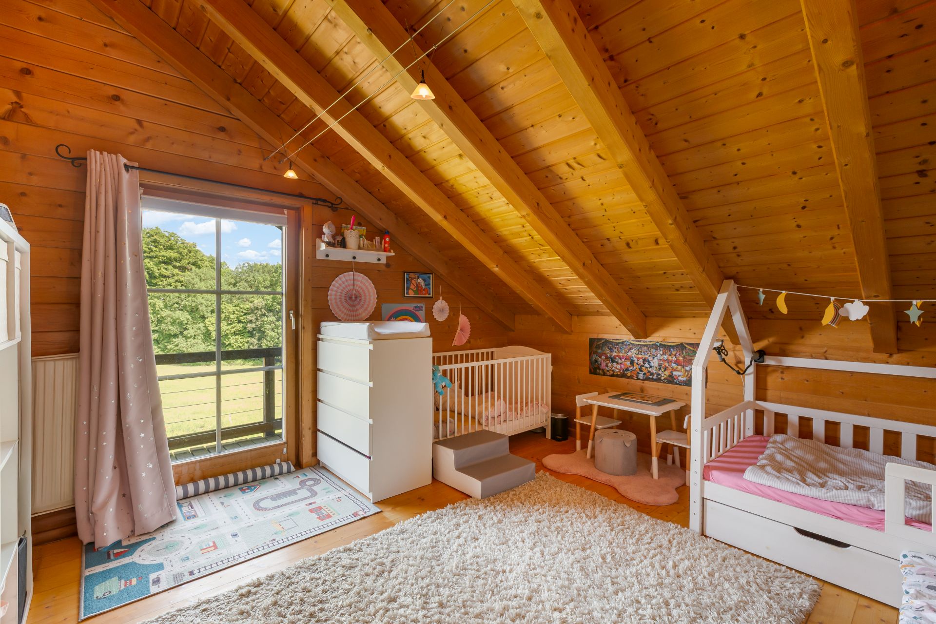 Kinderzimmer im Dachgeschoss mit Holzdecke, Teppich, zwei Betten und Spielbereich.