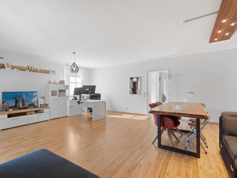 Helles Wohnzimmer mit Holzboden, Esstisch, Schreibtisch und Fernseher.