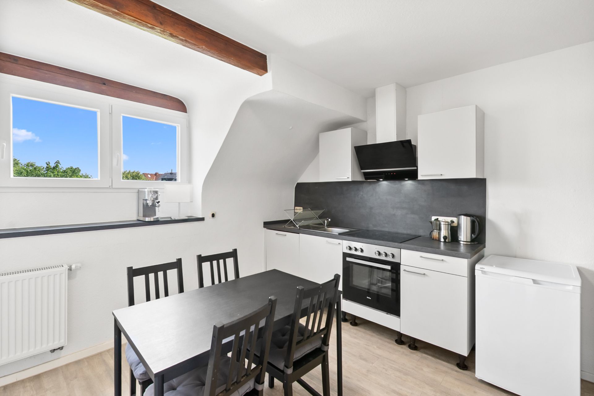 Moderne Küche mit Esstisch, Stühlen, Herd, Kühlschrank und zwei Fenstern.