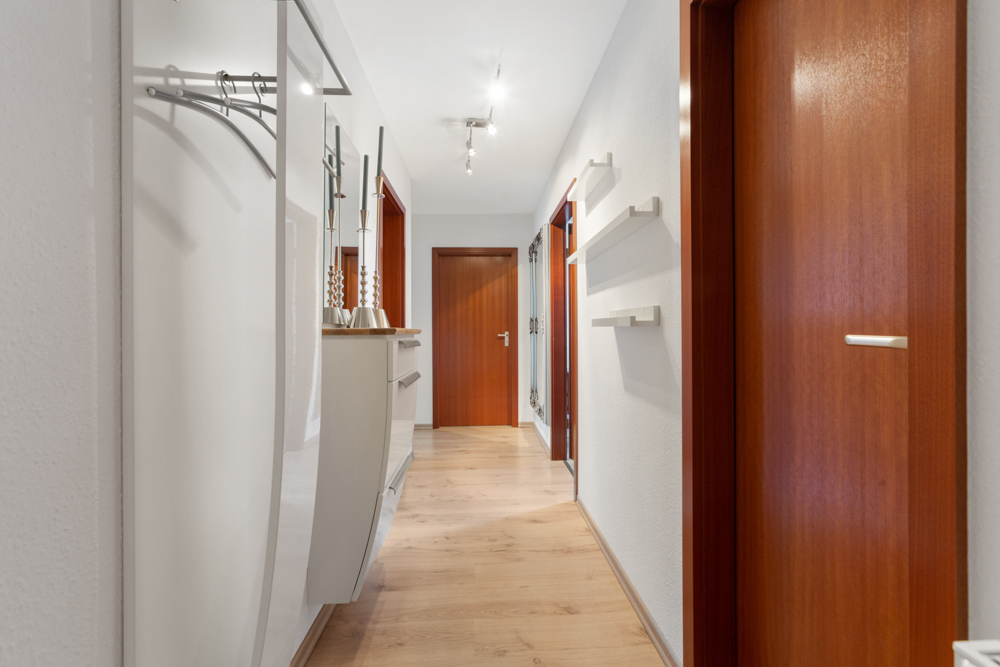 Heller Flur mit Holzfußboden, weißen Wänden und mehreren Holztüren.
