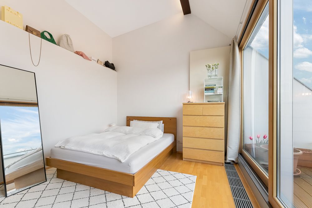Helles Schlafzimmer mit Holzbett, Kommode, großem Spiegel und Fensterfront.