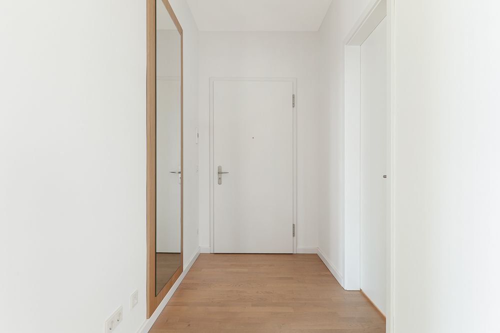 Heller Flur mit Holzboden, weißer Tür und großem Wandspiegel.