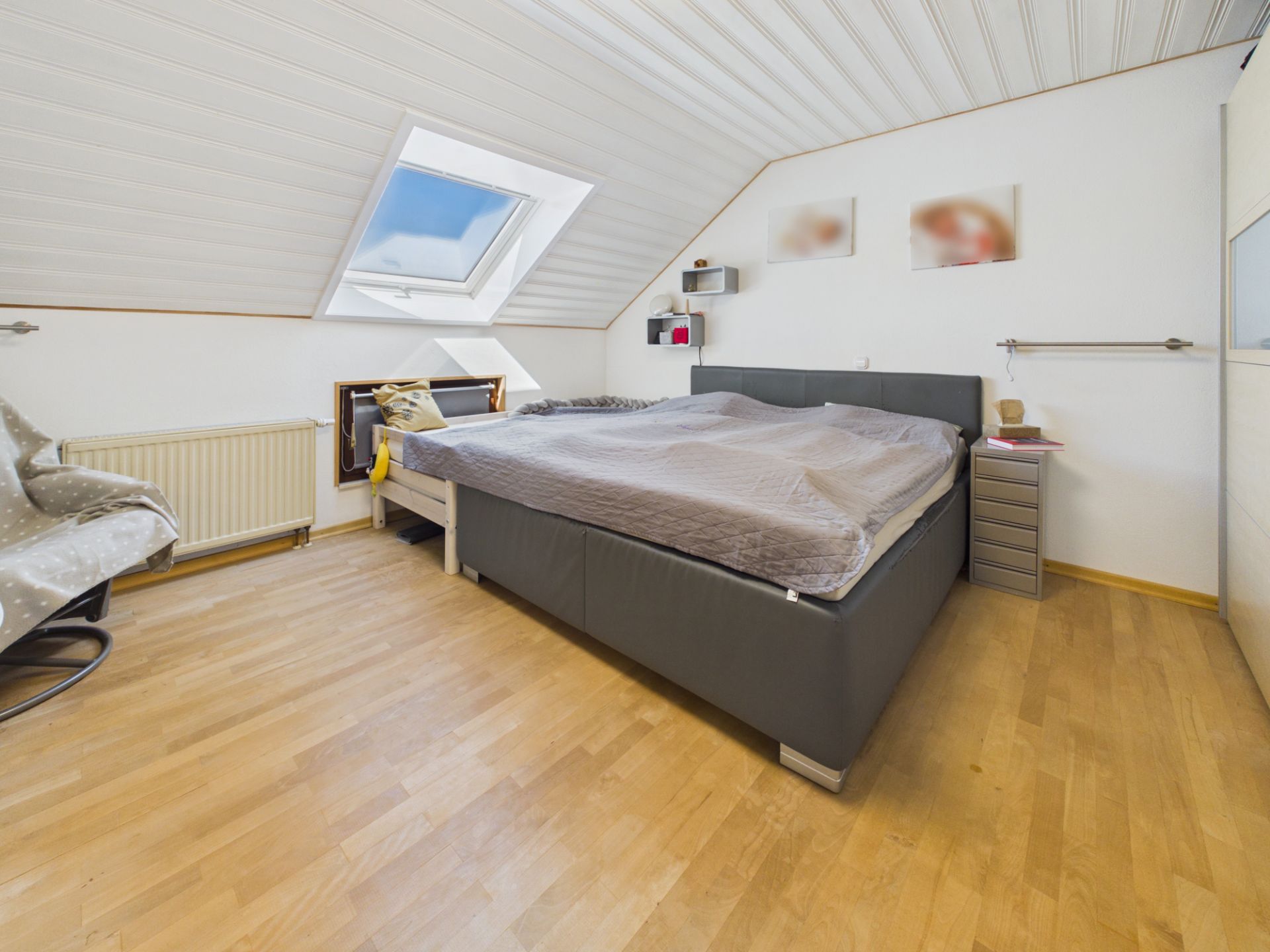 Schlafzimmer mit Doppelbett, Dachfenster und Holzfußboden unter schräger Decke.