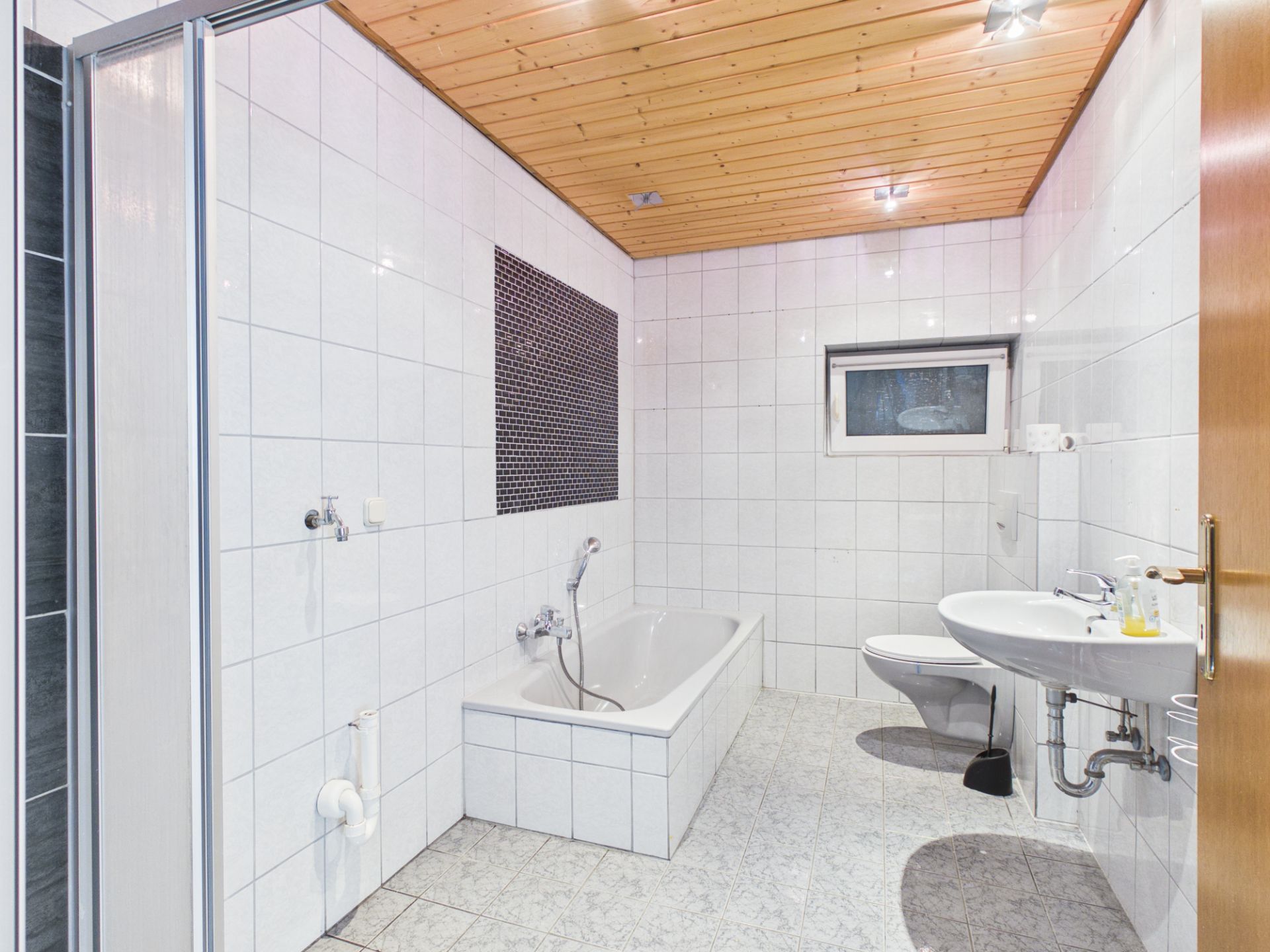 Helles Bad mit Badewanne, Waschbecken, Toilette, Fliesen und Holzdecke.