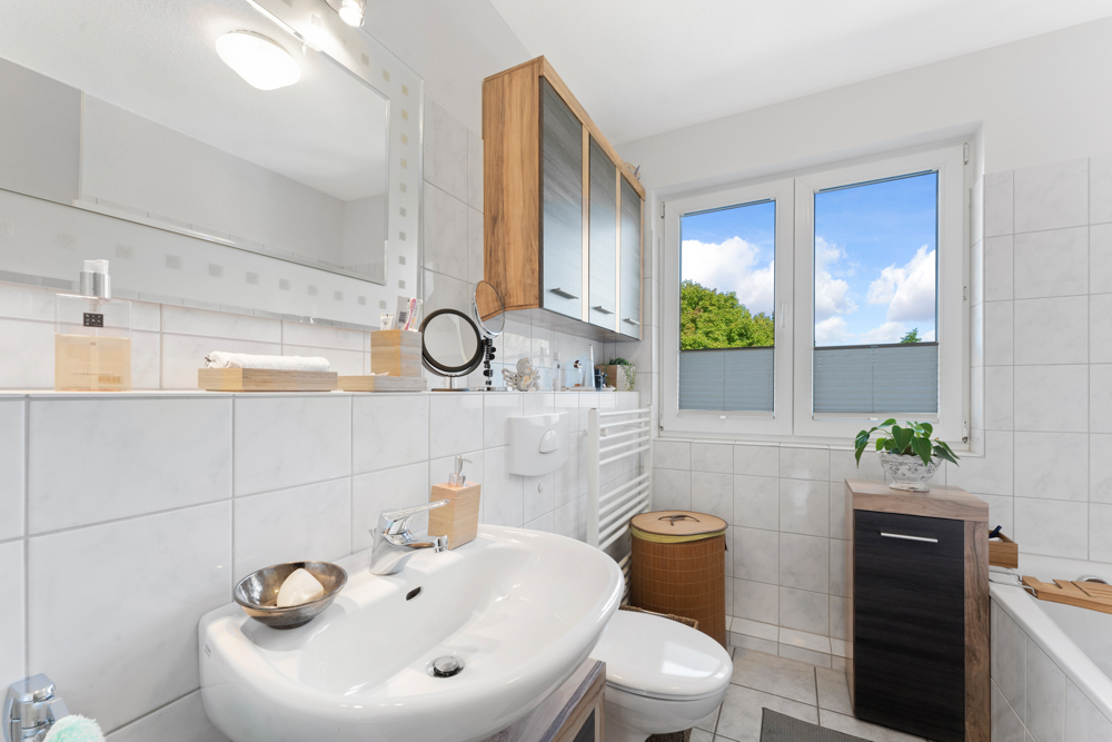 Modernes Badezimmer mit Waschbecken, Spiegel, Fenster und weißen Fliesen.
