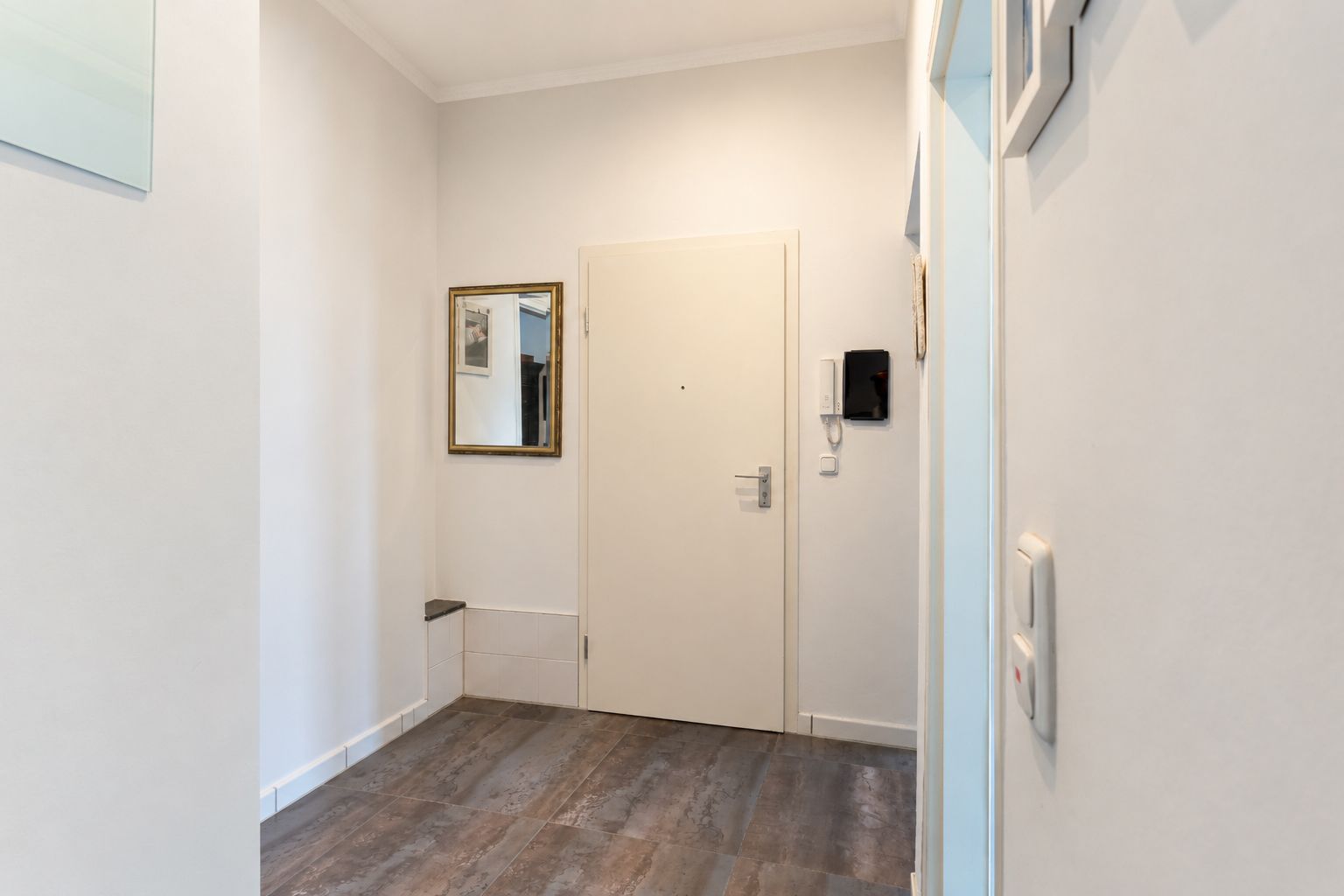 Heller Flur mit Eingangstür, Spiegel, Telefon und Fliesenboden.