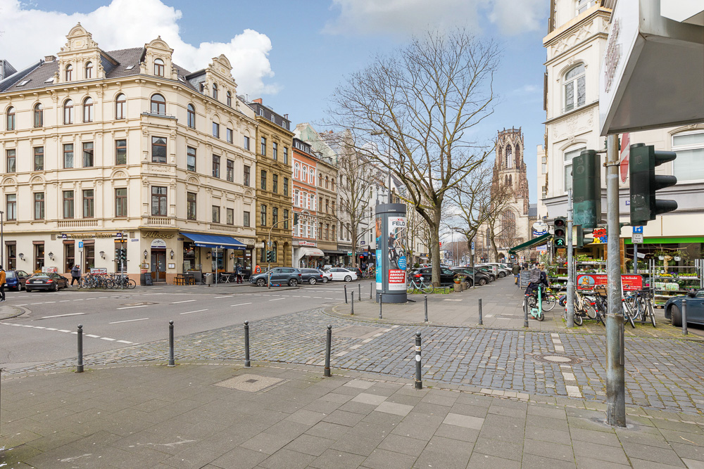 Stadtecke mit Altbauten, Geschäften, parkenden Fahrrädern und Bäumen auf dem Gehweg.