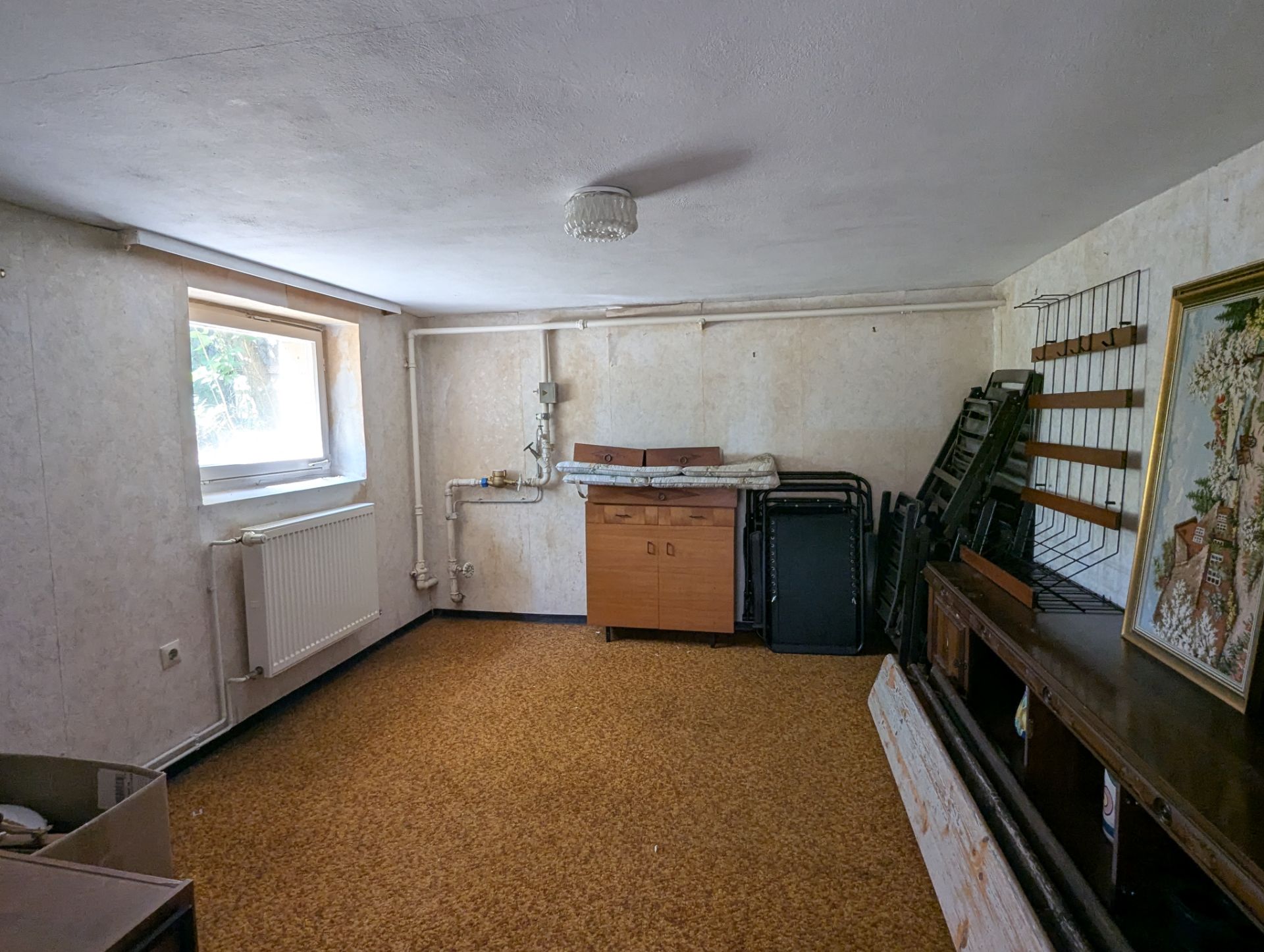 Kellerraum mit Fenster, Heizkörper, Schränken, Regalen und Teppichboden.