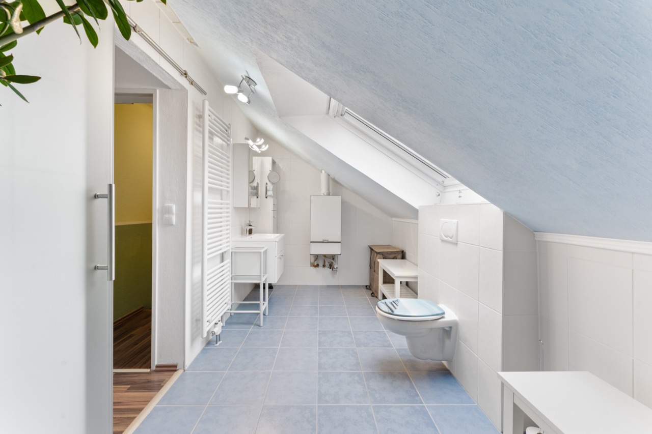 Modernes Dachgeschoss-Badezimmer mit blauen Fliesen, Wandtoilette und Dachfenster.