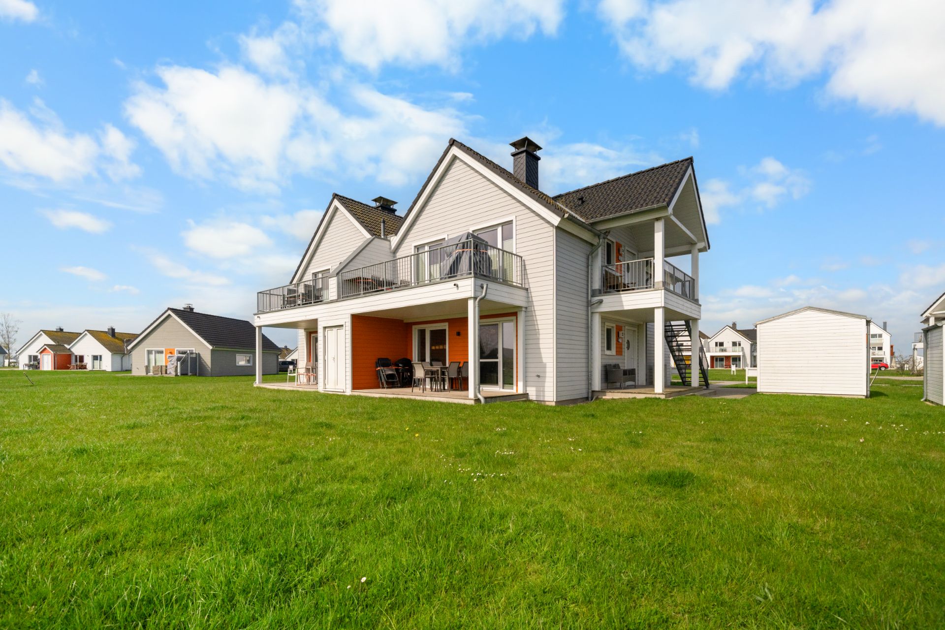 Modernes zweistöckiges Haus mit Balkonen und Terrasse auf einer großen grünen Wiese.