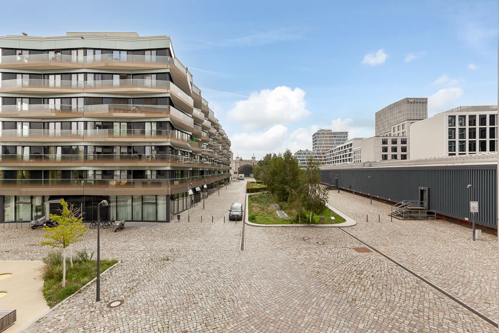 Moderner Wohnkomplex mit Balkonen und gepflastertem Hof, zentraler Grünfläche und einigen Bäumen.