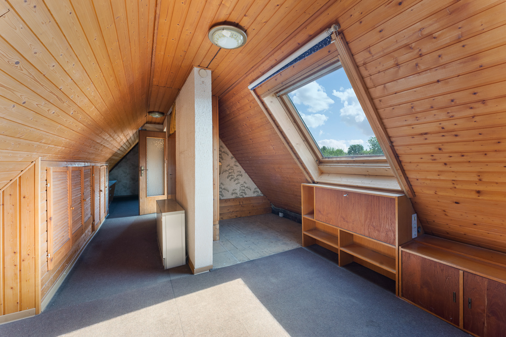 Dachgeschossraum mit Holzverkleidung, großem Fenster und eingebauten Schränken.