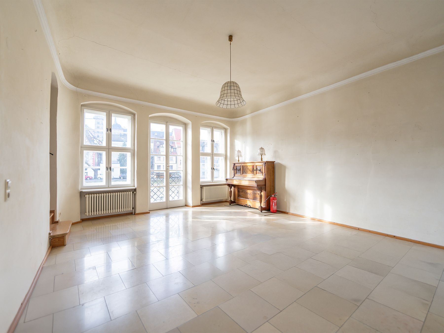Helles Wohnzimmer mit großen Fenstern, Fliesenboden und Klavier an der Wand.