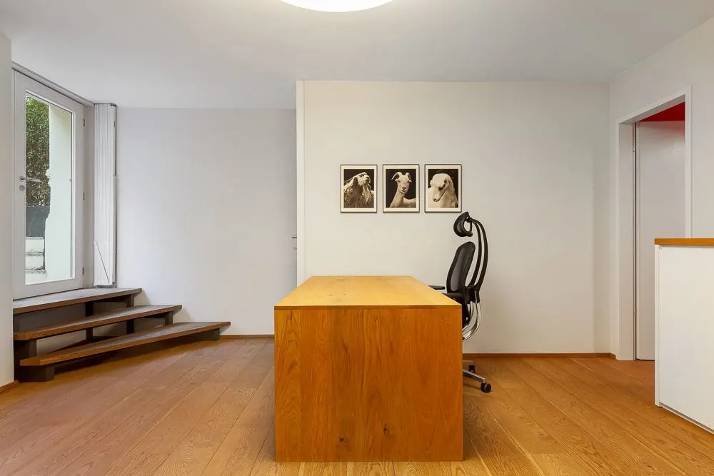 Helles Arbeitszimmer mit Holzschreibtisch, Bürostuhl und drei Bildern an der Wand.