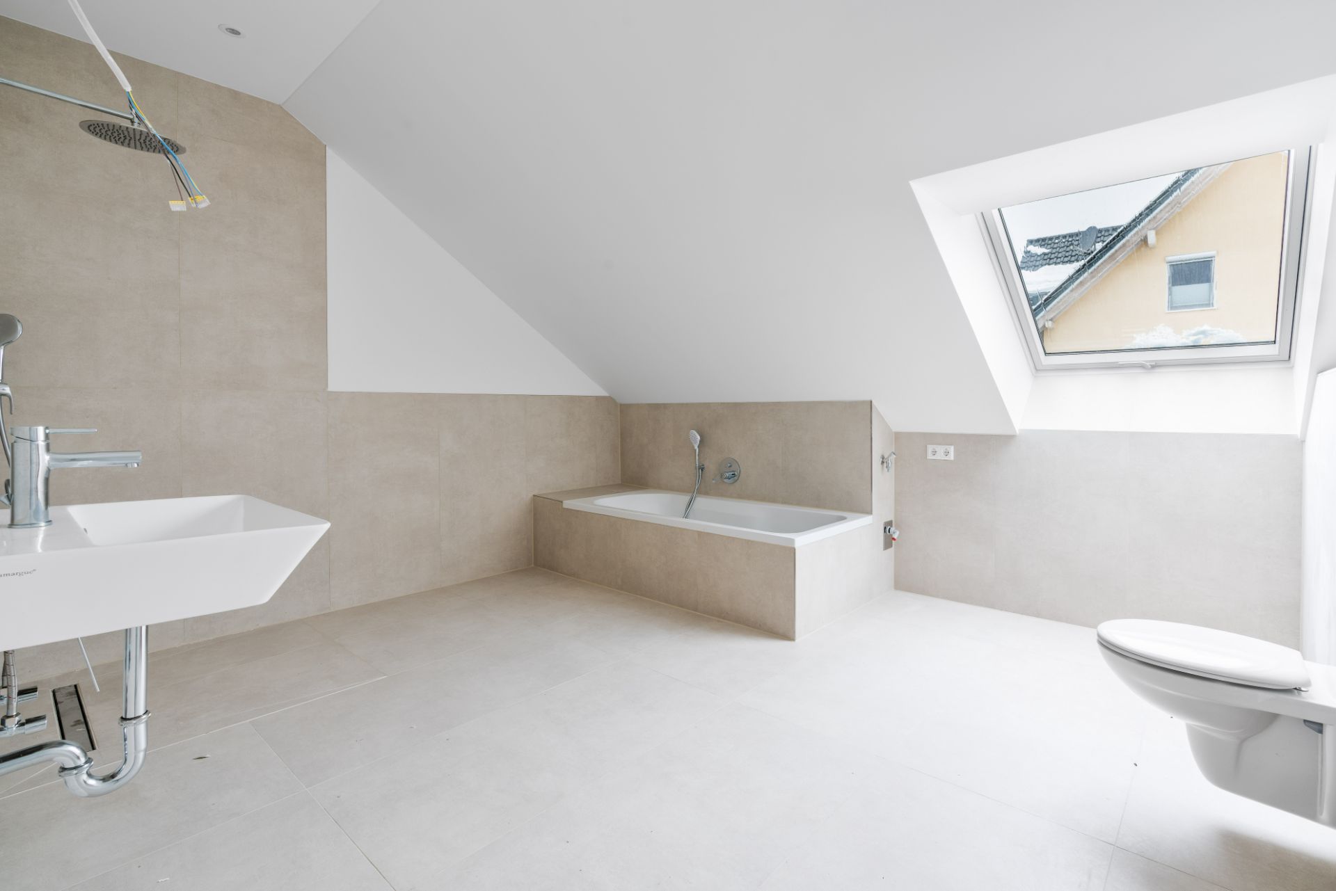 Modernes Badezimmer mit Badewanne, Waschbecken, Toilette und Dachfenster in einem Dachgeschoss.