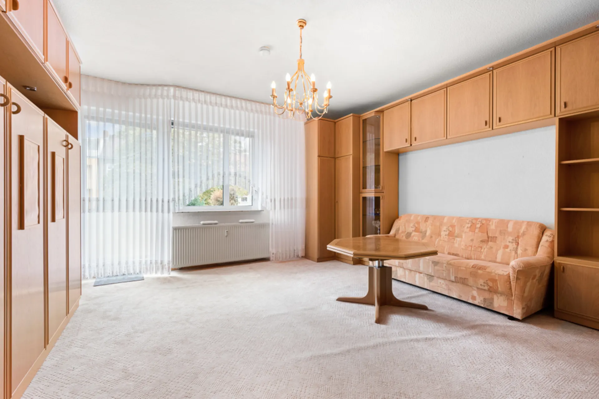 Helles Wohnzimmer mit Teppich, Holzmöbeln, Sofa, Couchtisch und Kronleuchter.