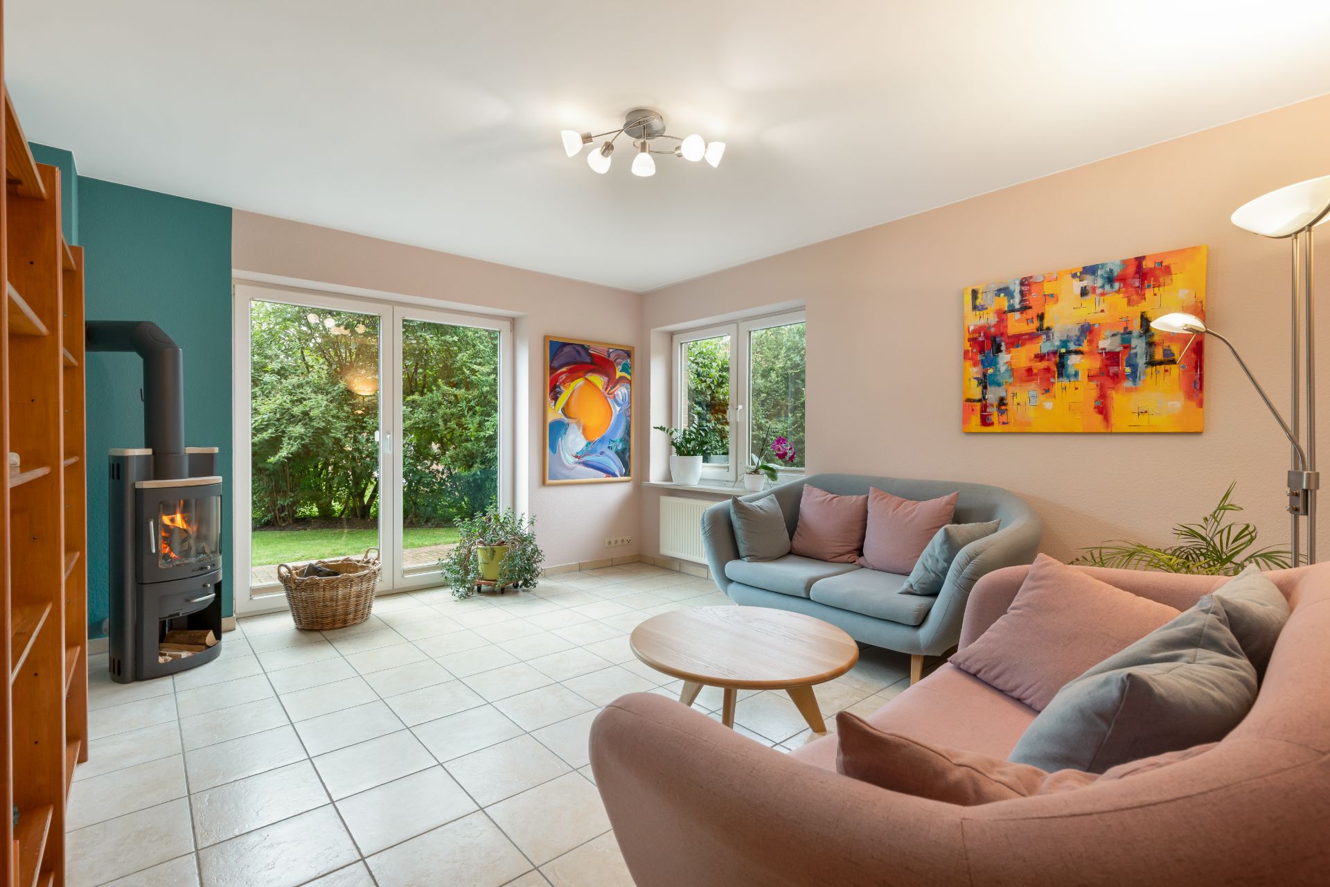 Helles Wohnzimmer mit zwei Sofas, Couchtisch, Kaminofen und bunten Bildern an den Wänden.