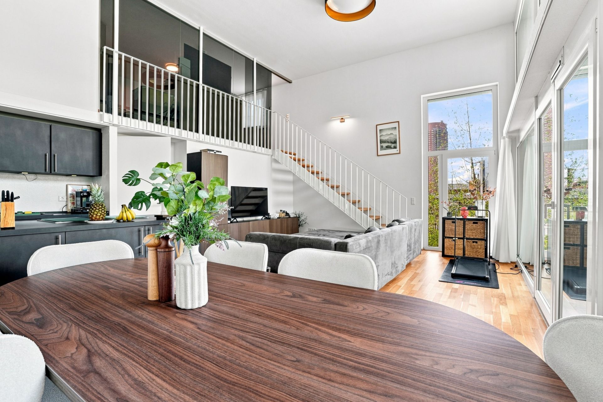 Modernes Wohnzimmer mit offener Küche, Esstisch, Sofa und Treppe zu einer Galerie.