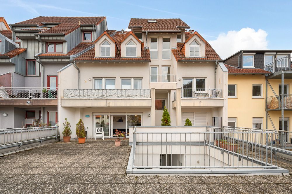 Wohnhaus mit Balkon, Terrasse und mehreren Fenstern, einige Pflanzenkübel auf der Terrasse.