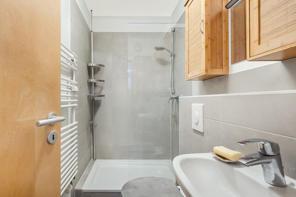 Modernes Badezimmer mit Dusche, Waschbecken, Handtuchheizkörper und Holzschränken.