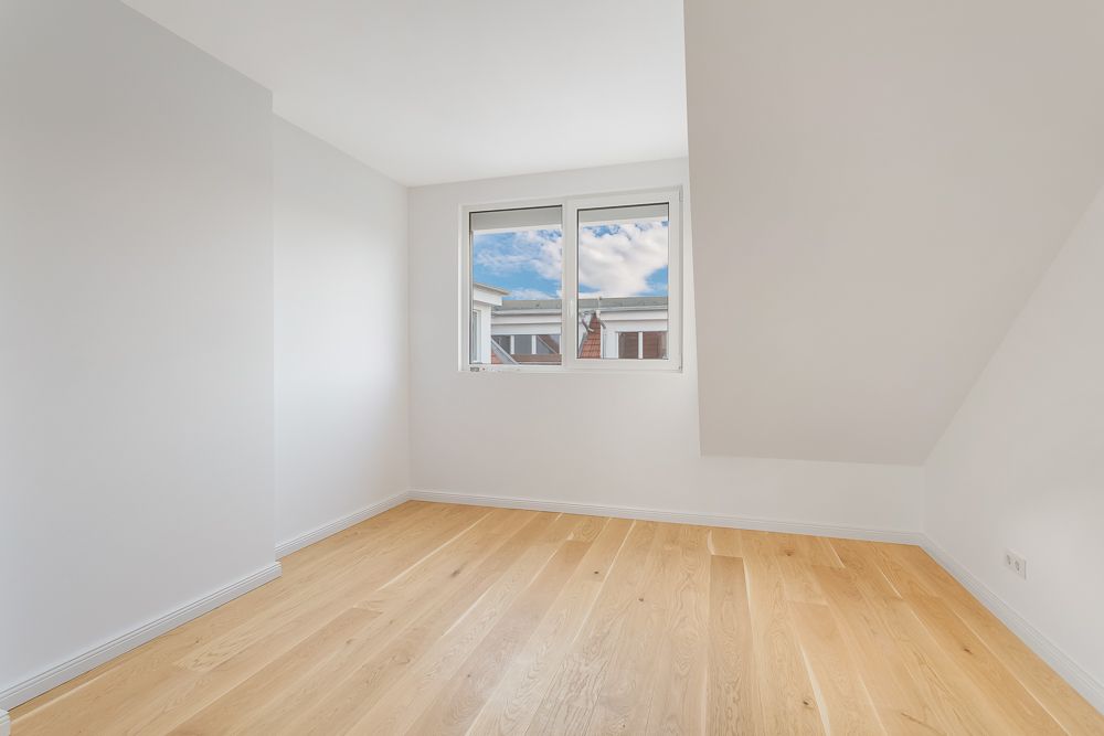 Heller Raum mit weiß gestrichenen Wänden, Holzboden und Fenster mit Blick nach draußen.
