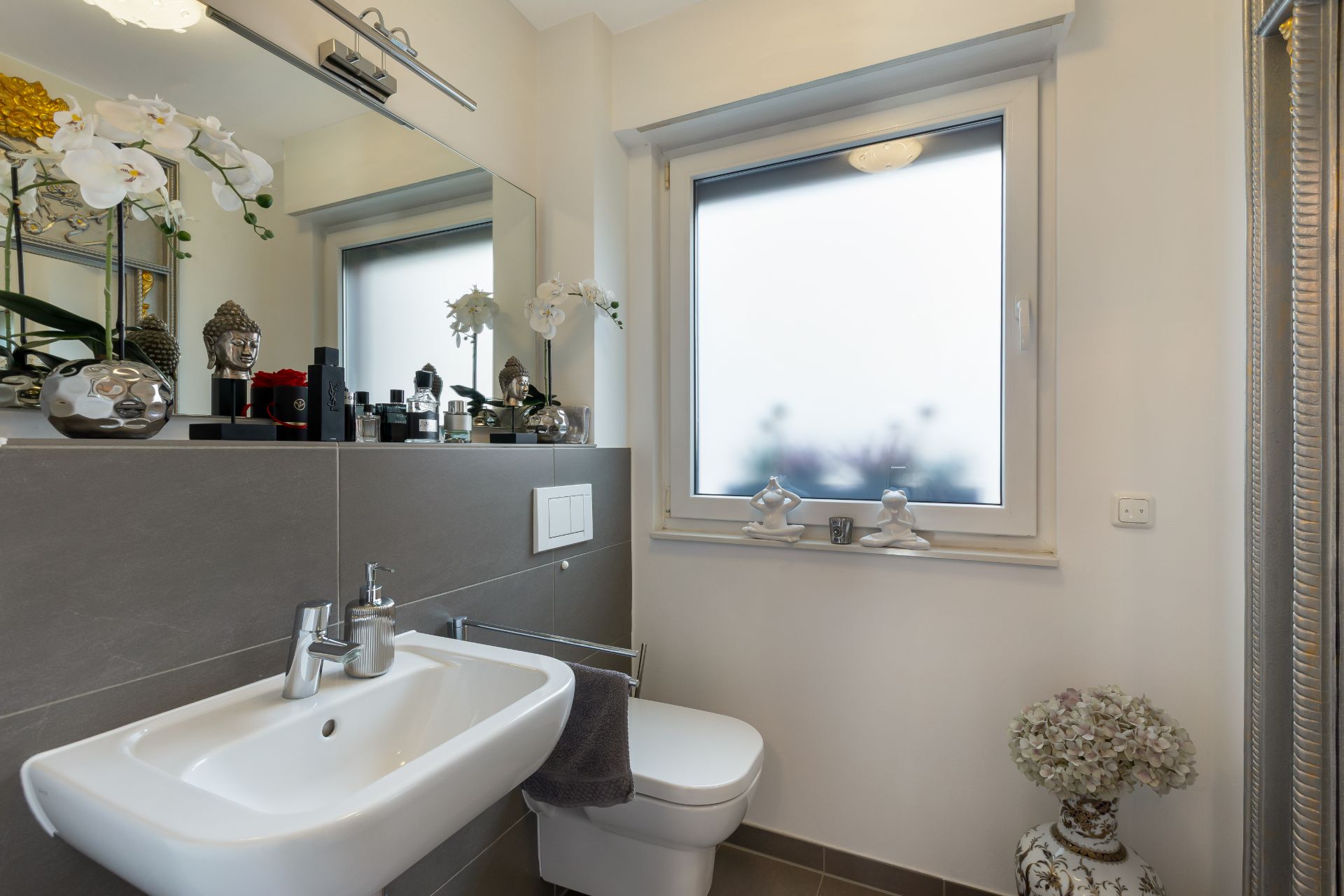 Modernes Badezimmer mit Waschbecken, WC, großem Spiegel und dekorierten Fensterbrett.