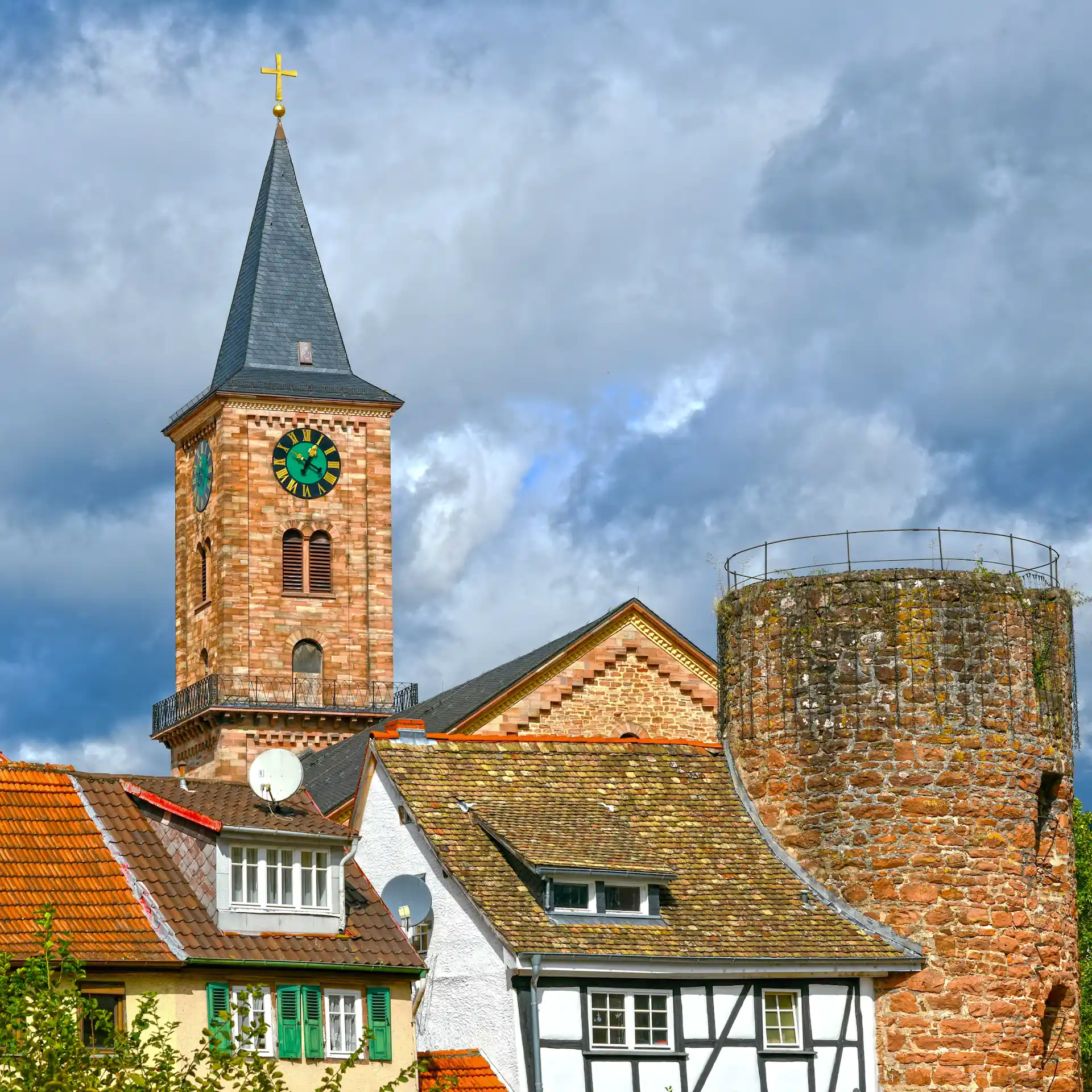Mehrere Häuser mit roten Dächern, Kirchturm und rundem Steinturm im Hintergrund.