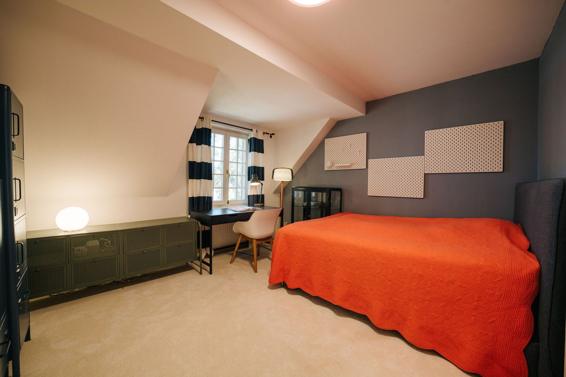 Schlafzimmer mit orangefarbener Decke, Schreibtisch am Fenster und moderner Einrichtung.