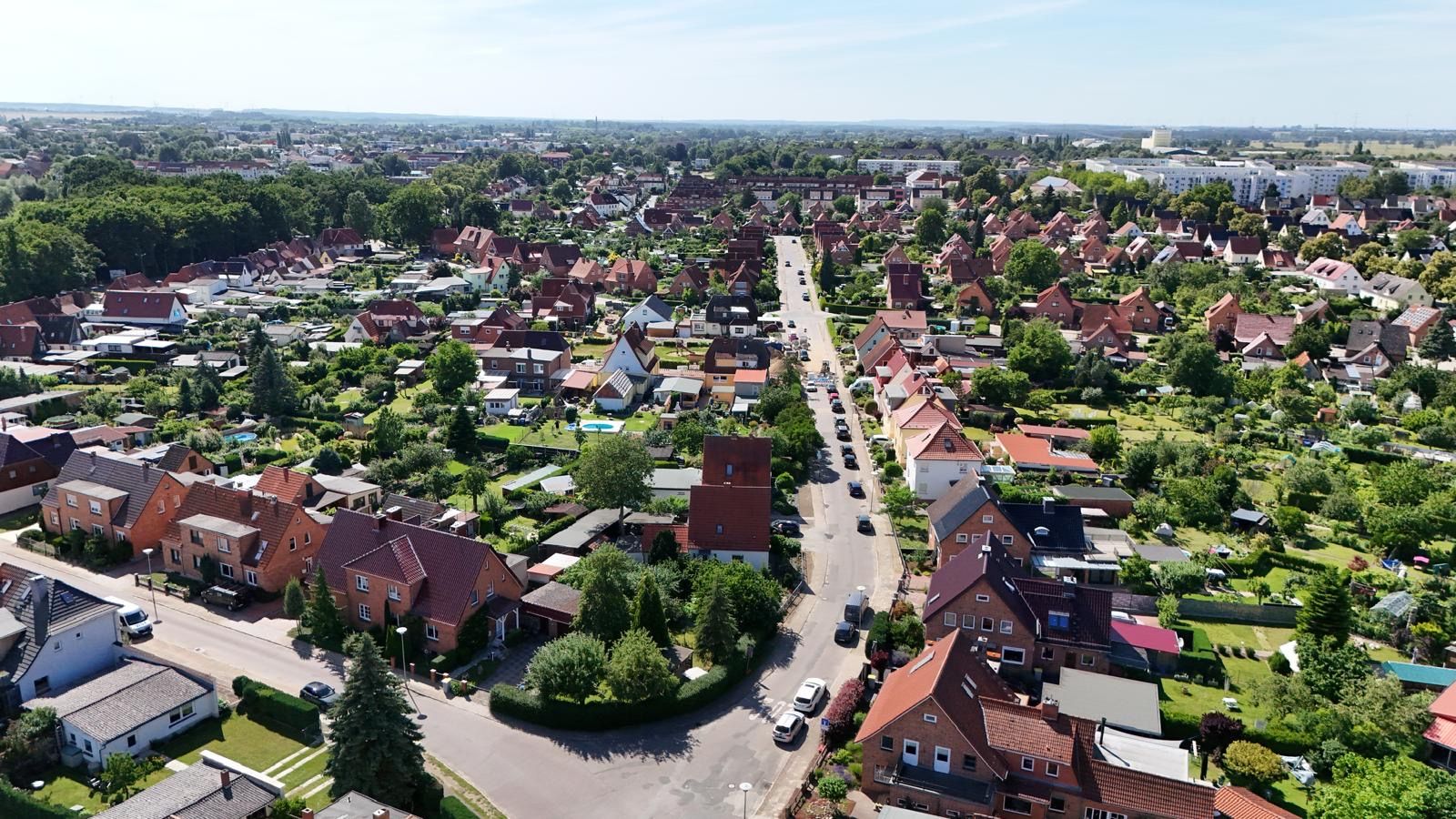 Luftaufnahme eines Wohngebiets mit Häusern, Gärten und einer Straße in der Mitte.