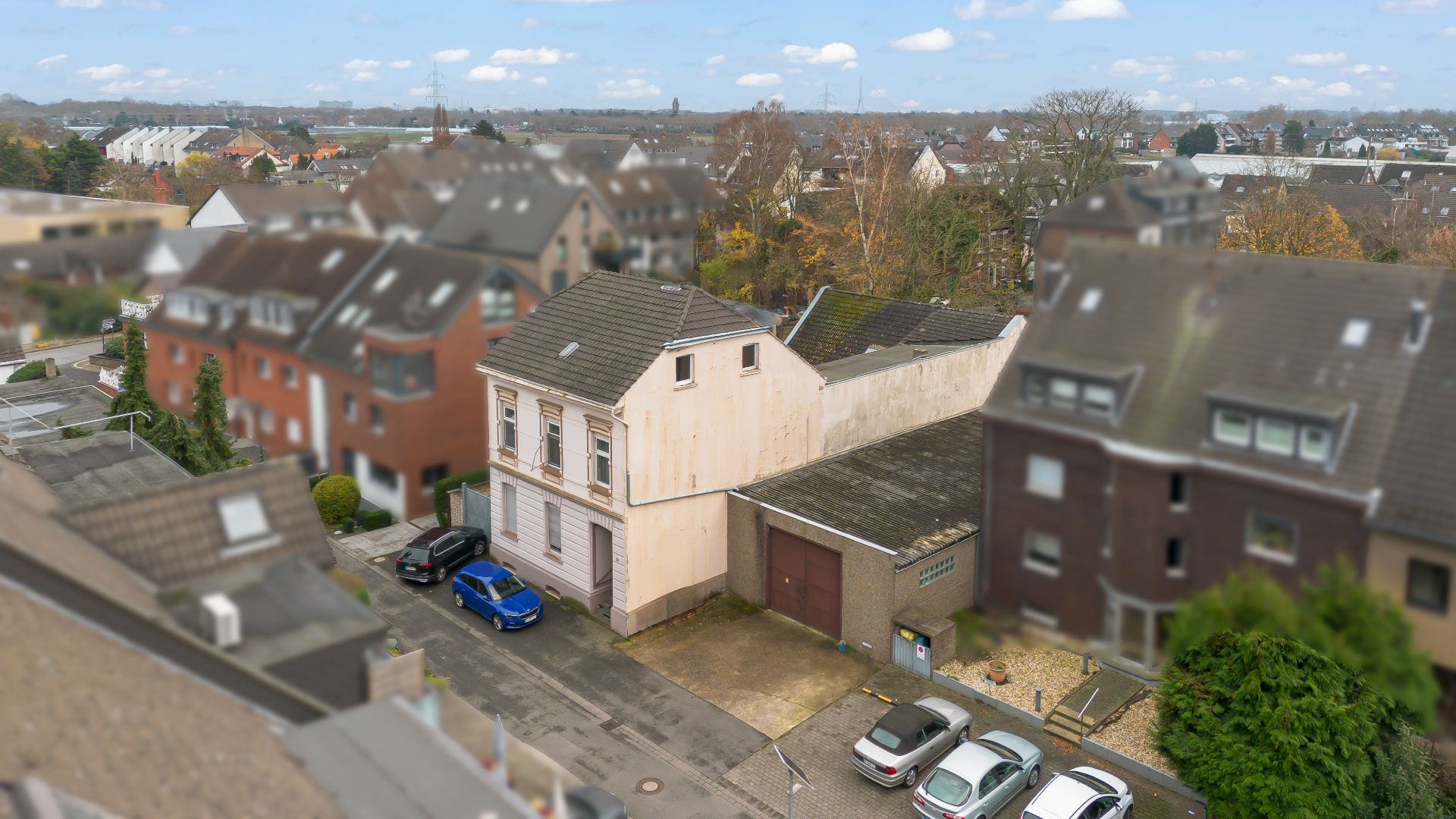 Mehrfamilienhaus mit Garage und geparkten Autos vor dem Gebäude, umgeben von weiteren Wohnhäusern.