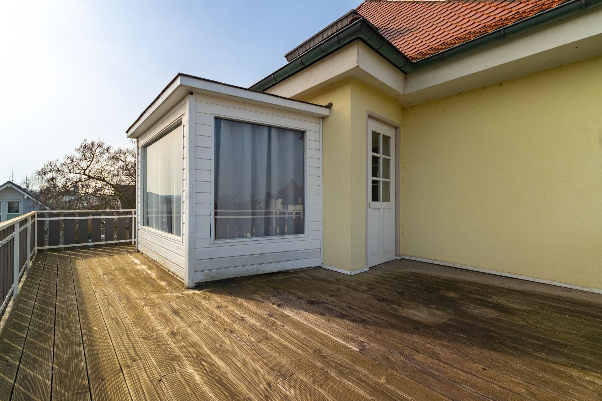 Große Dachterrasse mit Holzboden, Geländer und Zugangstür, daneben ein verglaster Erker.