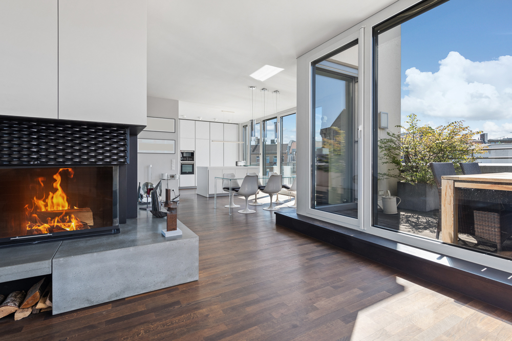 Modernes Wohnzimmer mit Kamin, offener Küche und Zugang zu einer Terrasse mit Esstisch.