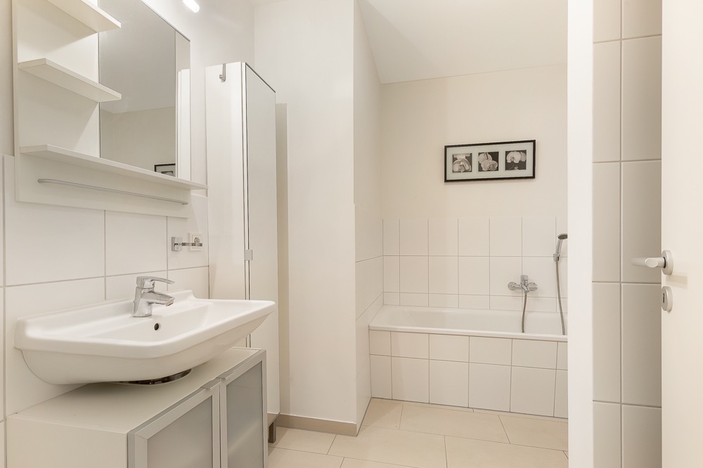 Helles Badezimmer mit Waschbecken, Badewanne, Spiegelschrank und Wandbild.
