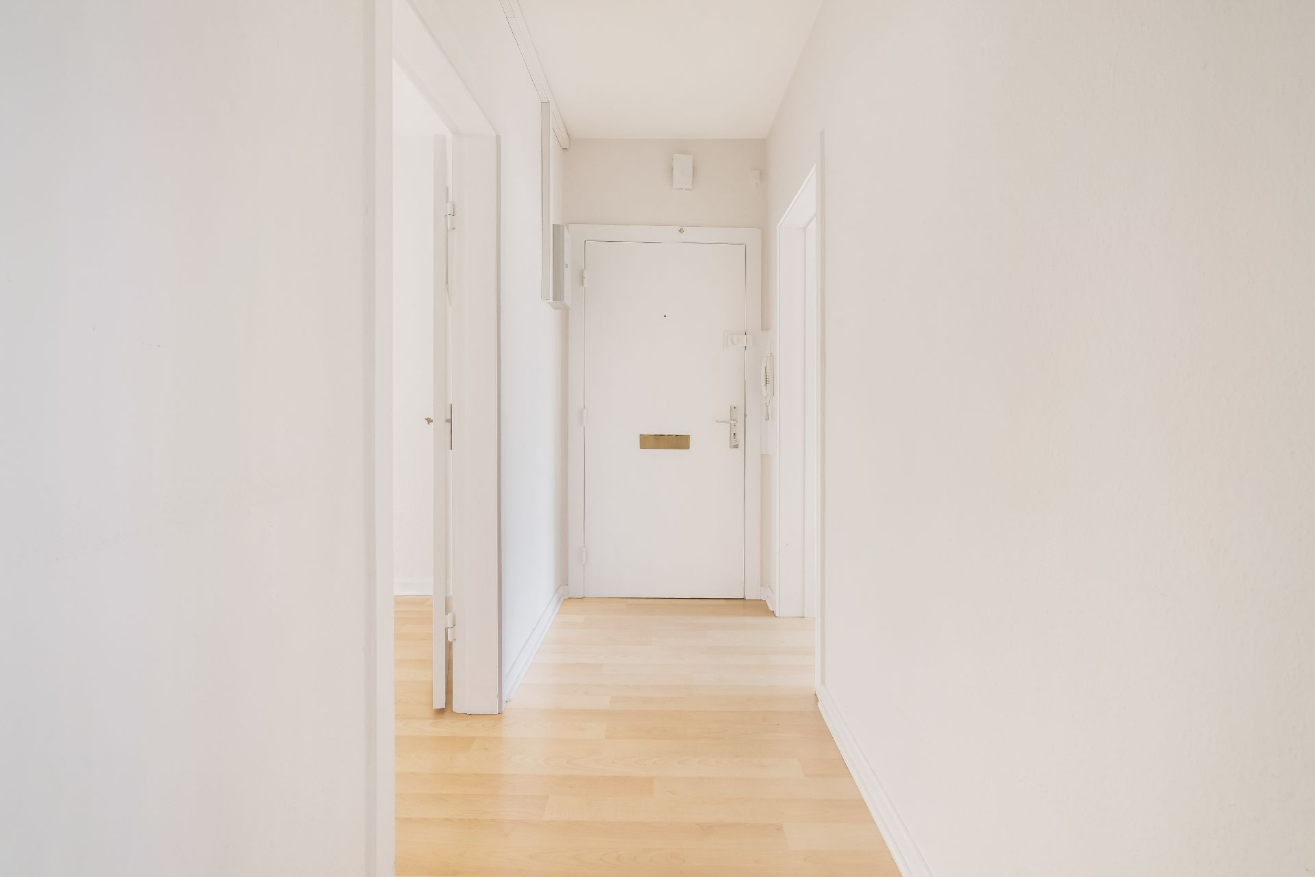 Heller Flur mit Holzboden und weißer Eingangstür in einer Wohnung.