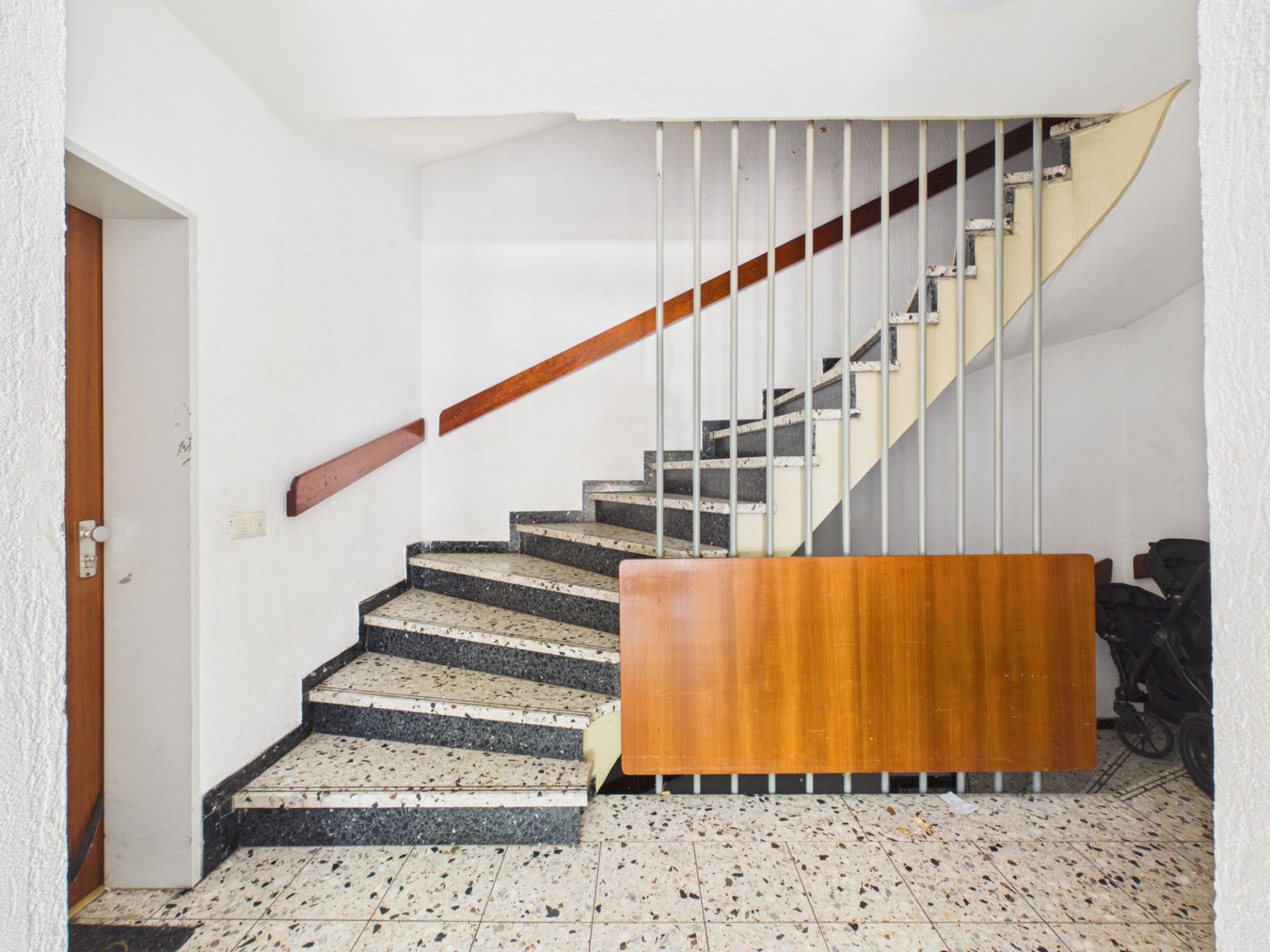 Treppenhaus mit gemusterten Stufen, Handlauf aus Holz und weißen Wänden.