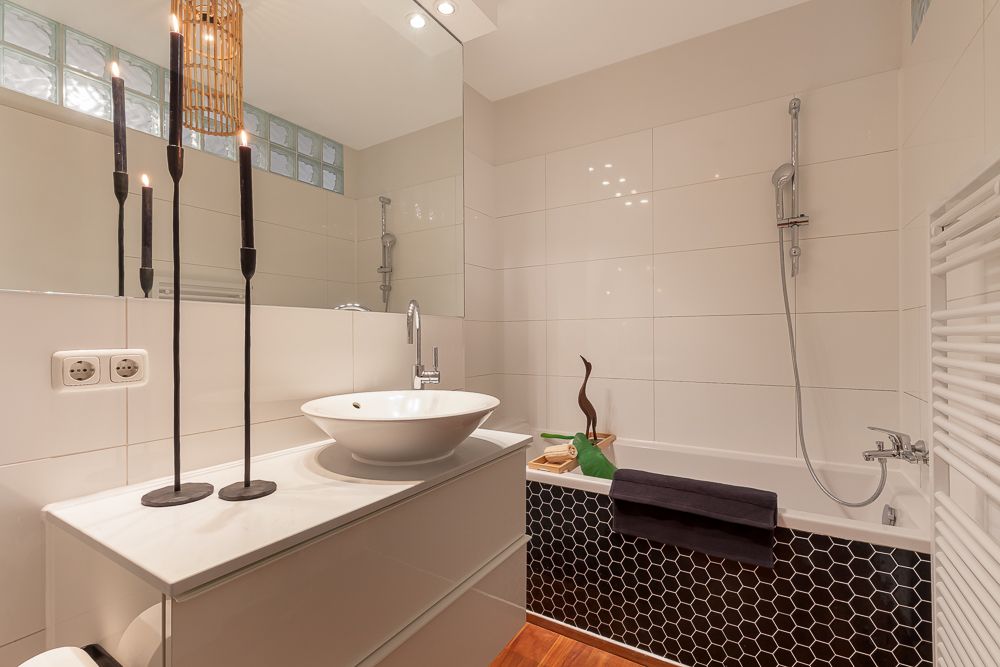 Modernes Badezimmer mit Waschbecken, Spiegel, Badewanne und schwarzen Deko-Kerzen.
