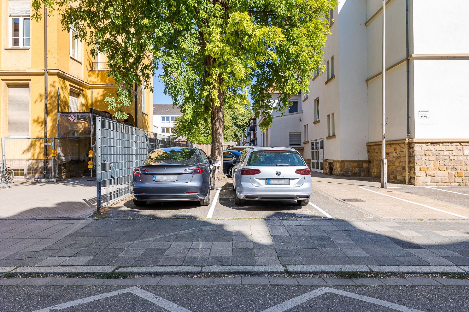 Zwei Autos parken nebeneinander auf einem Parkplatz neben Wohngebäuden und Bäumen.