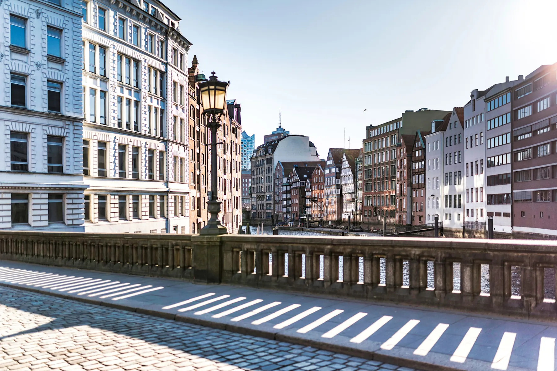 Brücke mit Laterne, im Hintergrund Wohnhäuser entlang eines Kanals bei Tageslicht.