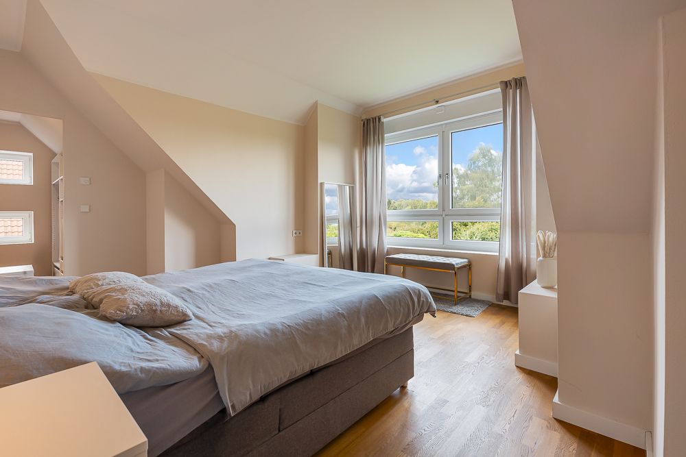 Helles Schlafzimmer mit großem Bett, Holzboden und Fenster mit Blick ins Grüne.