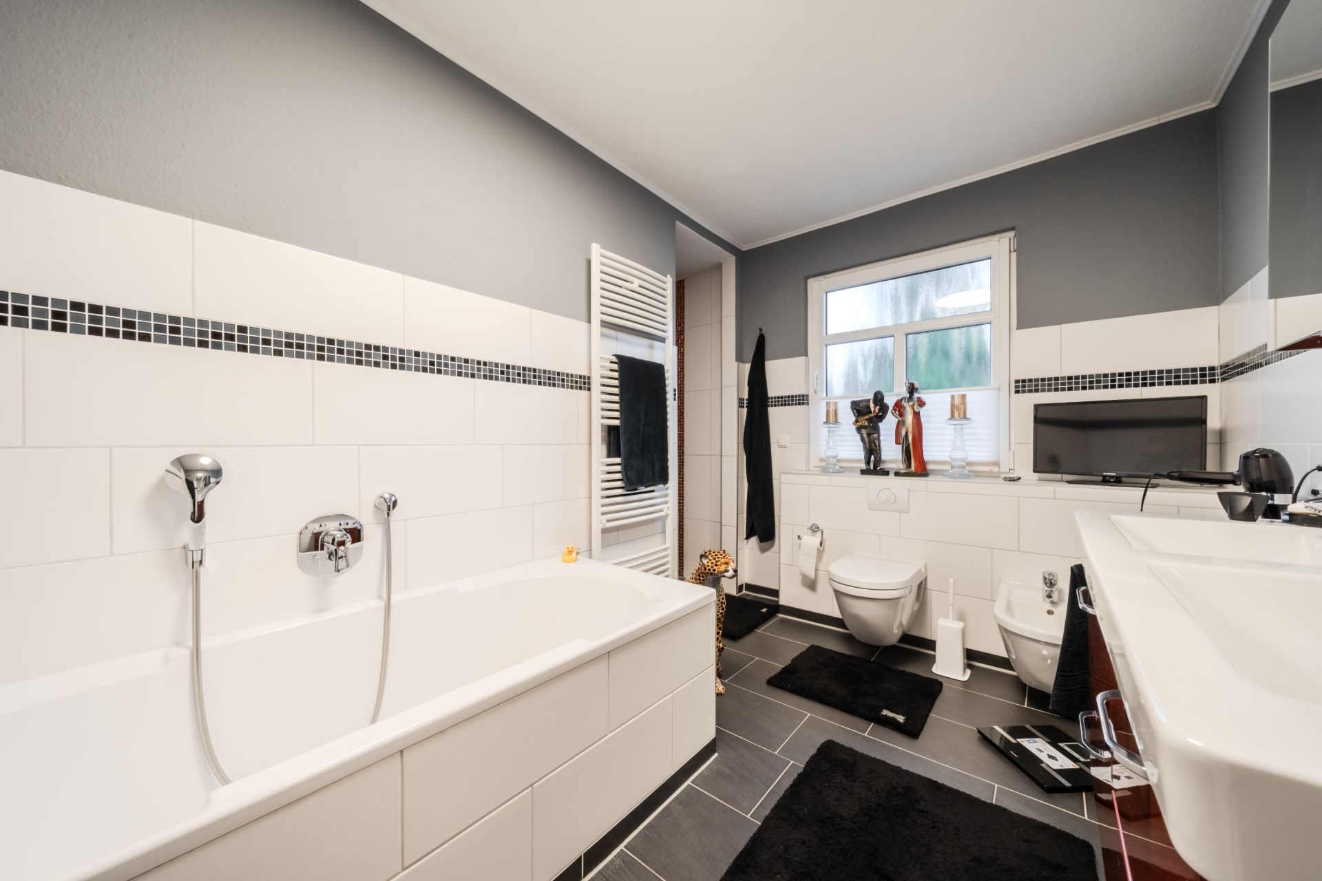Modernes Badezimmer mit Badewanne, Waschbecken, WC, Bidet und Fenster.