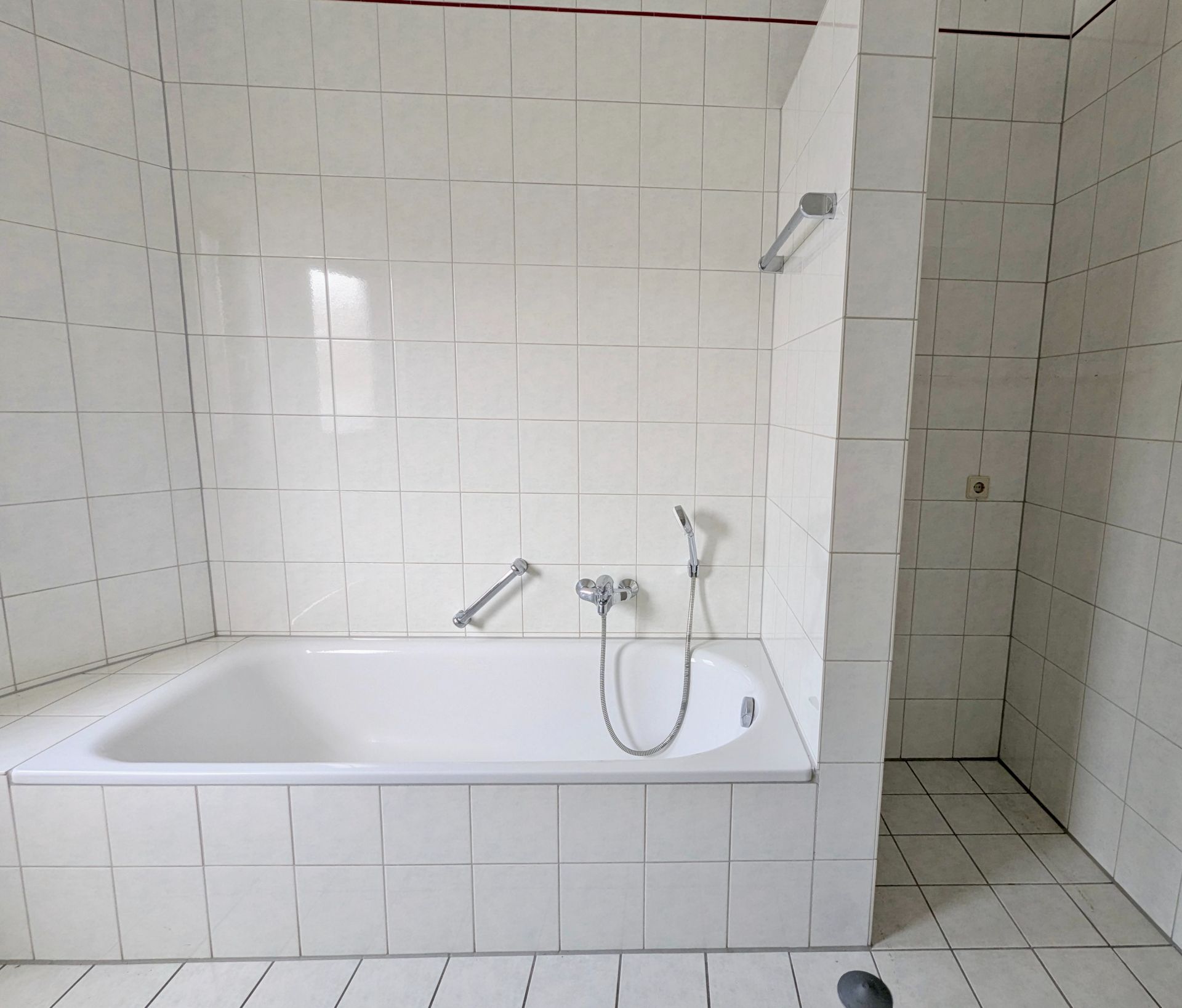 Weiß gefliestes Badezimmer mit Badewanne und abgetrenntem Duschbereich.