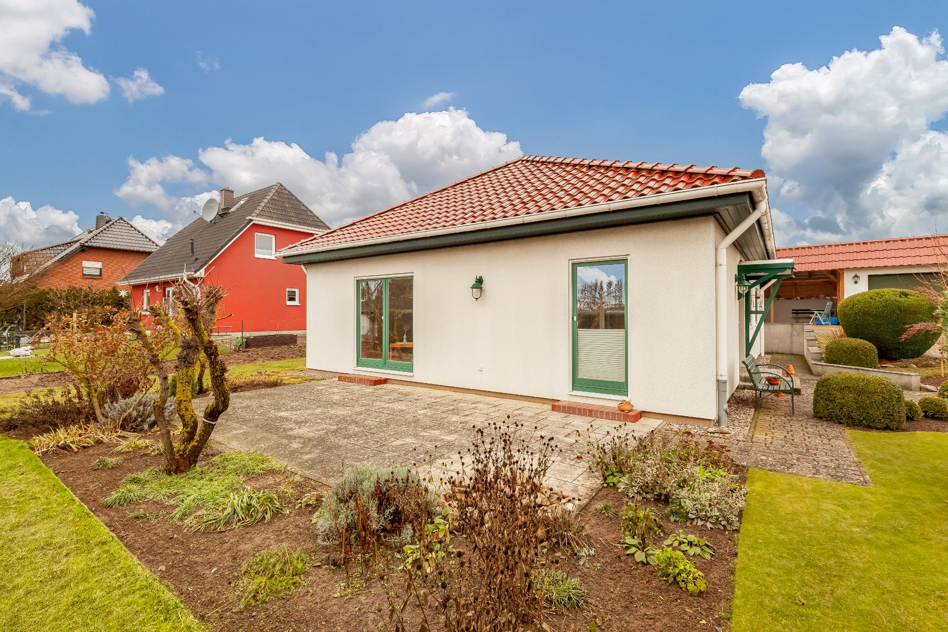 Einfamilienhaus mit rotem Dach, Terrasse und gepflegtem Garten bei blauem Himmel.