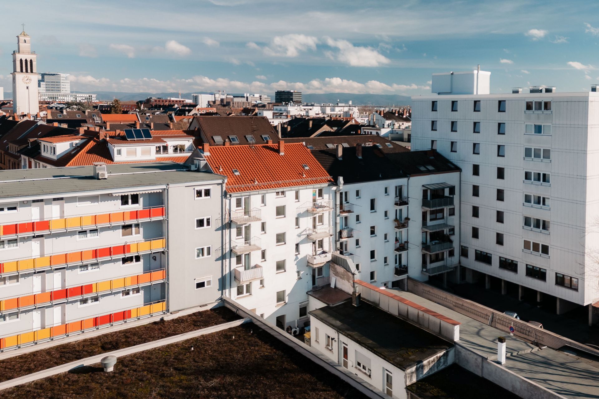 Blick auf mehrere Wohngebäude mit Balkonen und roten Dächern in einer Stadt.