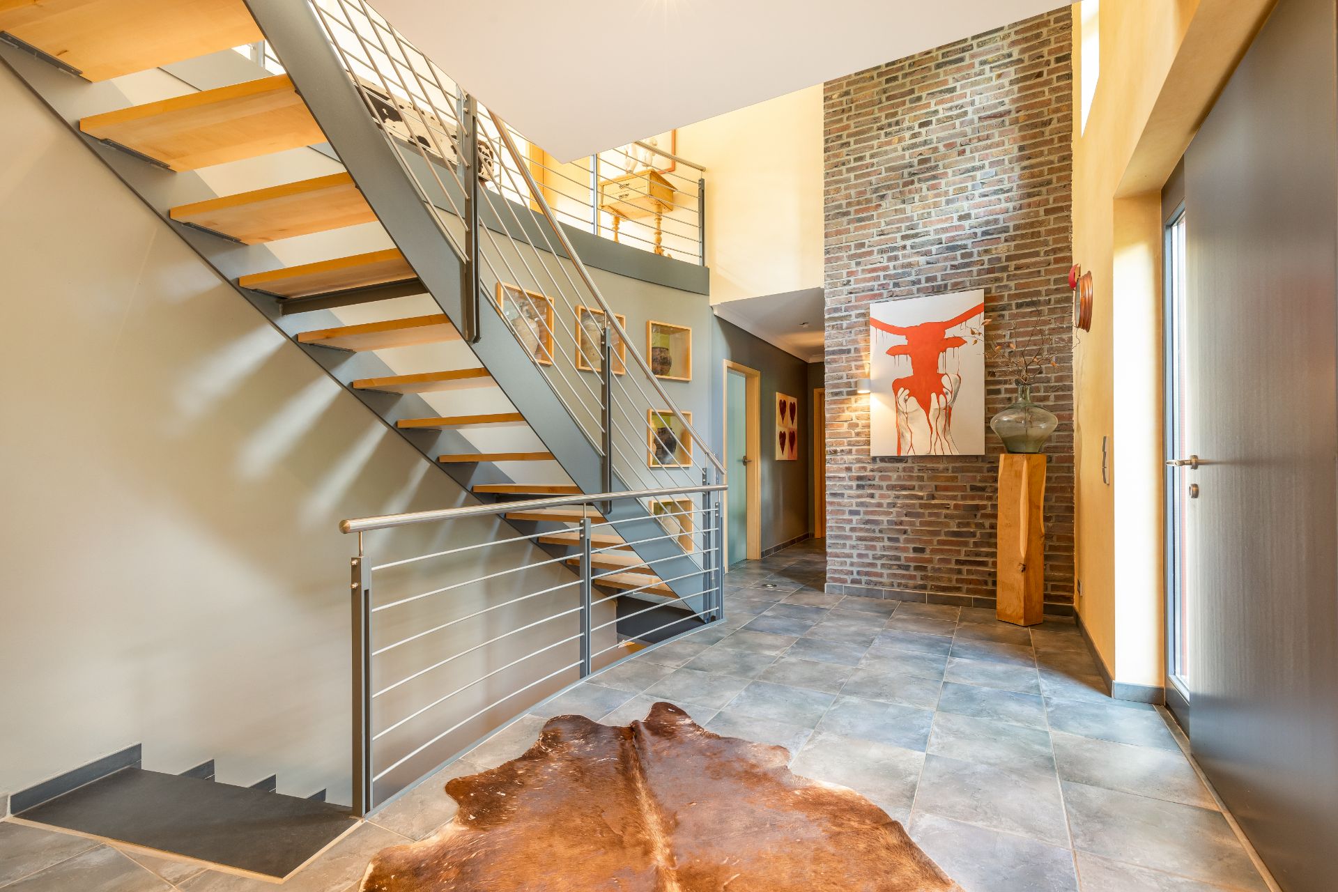 Heller Flur mit moderner Treppe, Kunst an der Wand und einem Tierfell-Teppich auf dem Boden.
