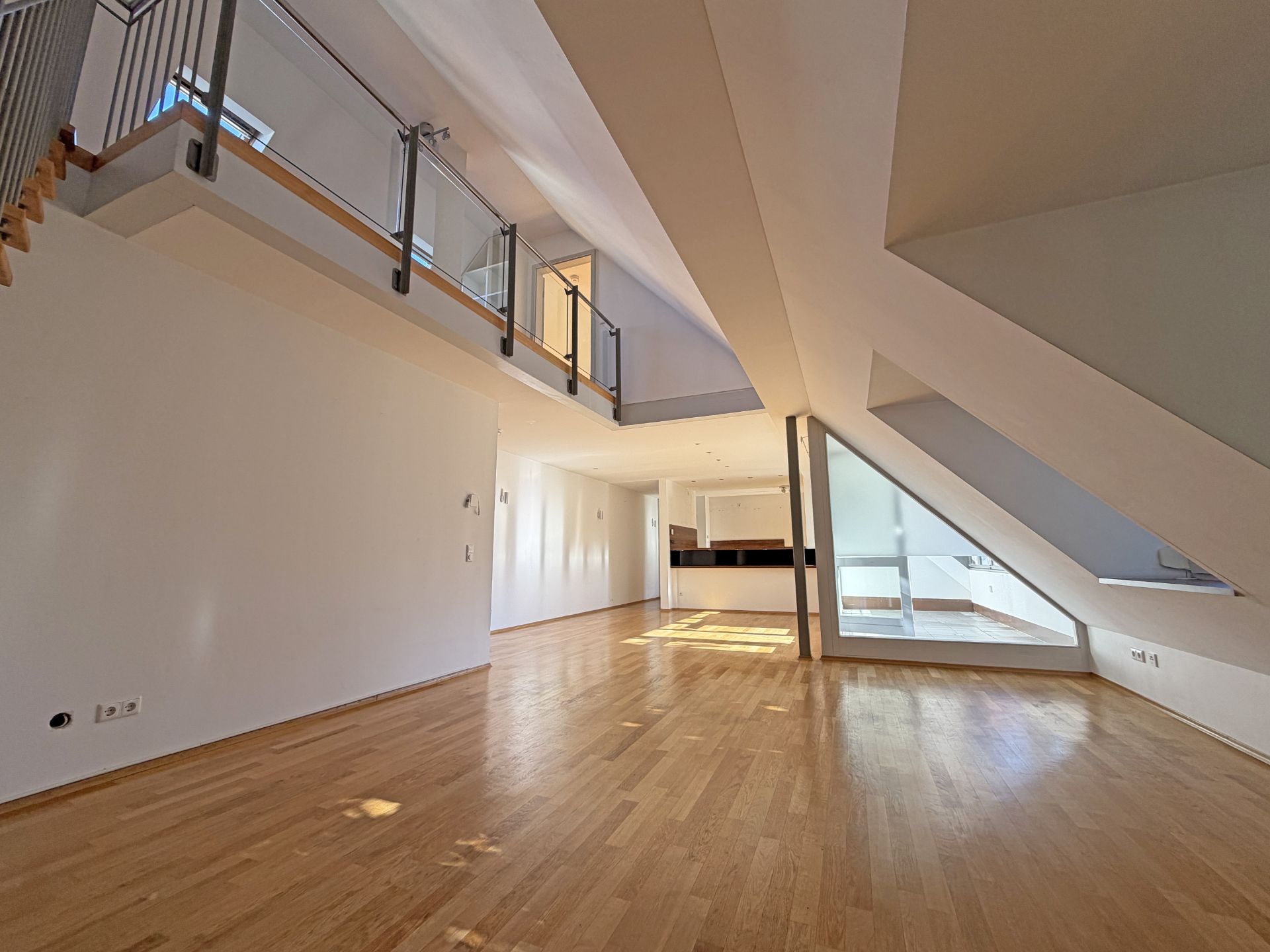 Helles Wohnzimmer mit Holzfußboden, Galerie und großen Fenstern unter einer schrägen Decke.